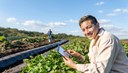 Young Hispanic farmer with digital tablet smiling in the fields. Japanese senior man working behind.